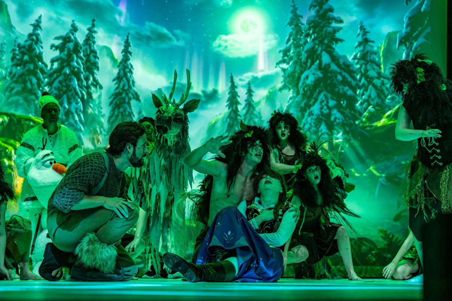 Anna, Kristoff, Olaf, and the Hidden Folk performing before Nick Carr Studio's projected forest environment